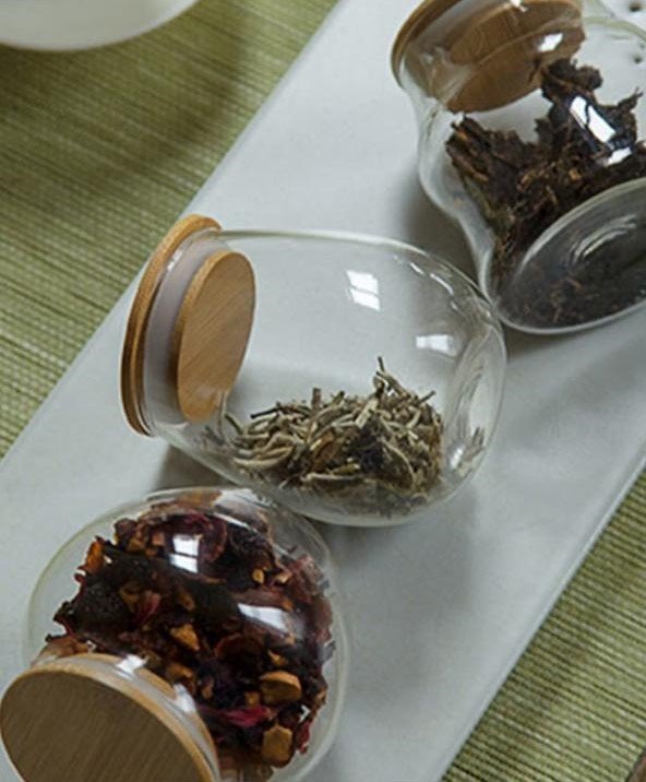 Clear glass jars with various dried herbs and spices on a wooden surface.