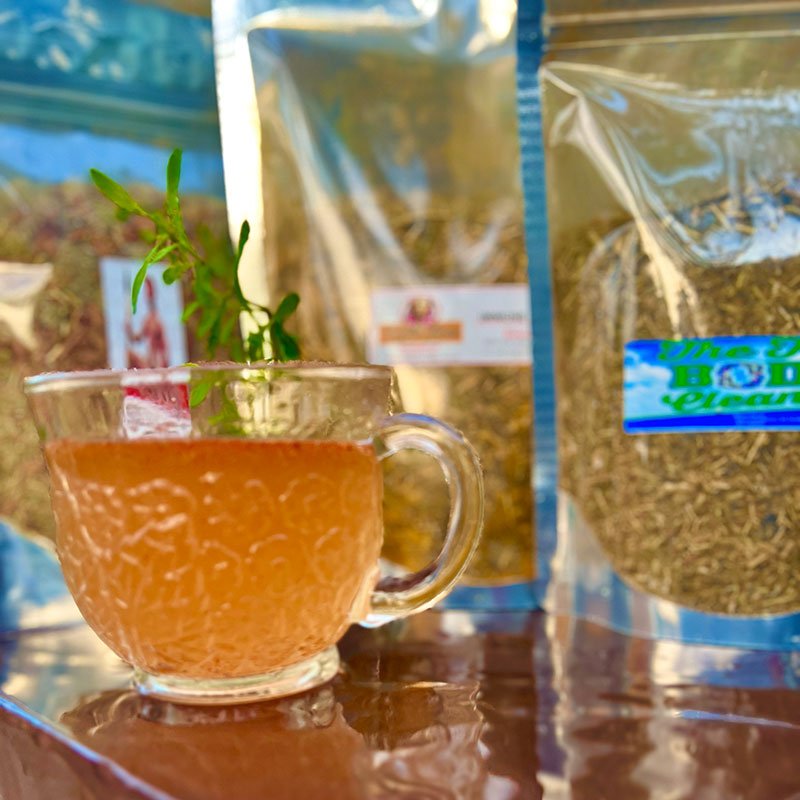 A glass cup of herbal tea with potted plants and packaged herbs.