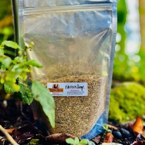 Clear pouch of dried herbs with a colorful label, placed outdoors among green plants.